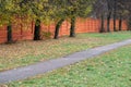 Asphalt footpath along the red fence and old trees, autumn, green lawn Royalty Free Stock Photo