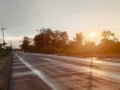 Asphalt paved road wet with rain on the side of the road beside the bush tree, Silhouette sunset shines bright orange color Royalty Free Stock Photo