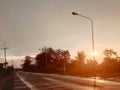 Asphalt paved road wet with rain on the side of the road beside the bush tree, Silhouette sunset shines bright orange color Royalty Free Stock Photo