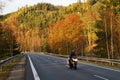 Asphalt road in the autumn landscape with a ride motorcycle, over the road forested mountain Royalty Free Stock Photo