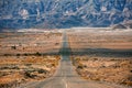 Asphalt road through a desert valley with mountains and canyons on the horizon