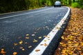 Asphalt  road at early autumn in the deciduous woods, passing car in the background Royalty Free Stock Photo