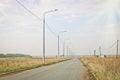 Asphalt road and lanterns on the side of the road and a lone cyclist in the distance in the warm sunshine.