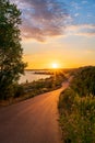 Asphalt road leading to a lake during a beautiful summer sunset