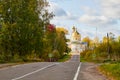 Asphalt road leading to the village with a beautiful white stone Orthodox Church with a yellow dome among nature and green trees. Royalty Free Stock Photo