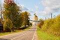 Asphalt road leading to the village with a beautiful white stone Orthodox Church with a yellow dome among nature and green trees. Royalty Free Stock Photo