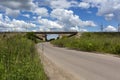 Asphalt road leads to the railway bridge, sky, clouds, grass Royalty Free Stock Photo