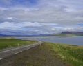 Asphalt road line through rural north summer landscape with green grass. colorful cliffs, lake, blue mountains and Royalty Free Stock Photo