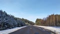 Asphalt road with markings passes through a wooded area. On the sides of the road are pine and birch trees. In winter, there is sn Royalty Free Stock Photo