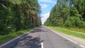 An asphalt road with markings goes through a mixed forest. The weather is sunny and the sky is blue with clouds Royalty Free Stock Photo