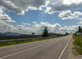 Asphalt road in mountain hilly countryside in pine forests, on background of blue sky with clouds, Ukraine, Carpathians