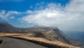 Asphalt road over a cliff above the ocean disappearing over the horizon through volcano mountain hillsides. White clouds on a blue Royalty Free Stock Photo