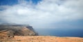 Asphalt road over a cliff above the ocean disappearing over the horizon through volcano mountain hillsides. White clouds on a blue Royalty Free Stock Photo