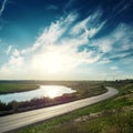 Asphalt road and river along it at sunset with clouds Royalty Free Stock Photo