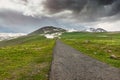 Road in rough terrain with snow-capped mountains and lush green meadows. The concept of travel in Iceland and the Nordic