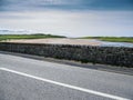 Asphalt road and stone fence. Green fence and sandy beach with small river, blue cloudy sky. West of Ireland. Irish landscape. Royalty Free Stock Photo