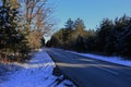 Asphalt road surrounded by winter mixed forest, mostly pine and other coniferous trees.