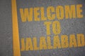 asphalt road with text welcome to Jalalabad near yellow line