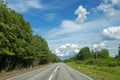 Asphalt road among the trees and blue sky with clouds