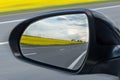 Asphalt road, yellow flowering fields and cloudy sky are reflected in the car mirror Royalty Free Stock Photo