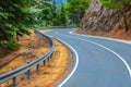 Asphalt serpentine road in Troodos mountain range with roadside fence and trees