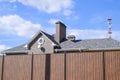 Asphalt shingle. Decorative bitumen shingles on the roof of a brick house. Fence made of corrugated metal.