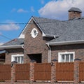 Asphalt shingle. Decorative bitumen shingles on the roof of a brick house. Fence made of corrugated Royalty Free Stock Photo