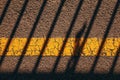Asphalt sidewalk surface with worn yellow line and striped shadow striped pattern as background
