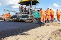 Asphalt spreader, tarmac road laying machine. Workers realign hot asphalt