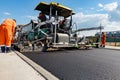 Asphalt spreader, tarmac road laying machine. Workers realign hot asphalt