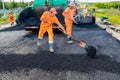 Asphalt spreader, tarmac road laying machine. Workers with shovels realign hot asphalt