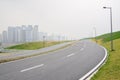 Asphalted road and sidewalk on grassy acclivity with city buildings in mist Royalty Free Stock Photo