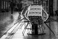 Assembled chairs from sidewalk cafÃÂ© in a rainy street and pedestrians from behind passing by, city life image in black and white