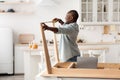 Assembling furniture. Excited african american man measuring the width between legs of wooden table in kitchen interior