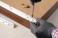 Assembling furniture, gloved hands set roller guides on drawer box, close-up