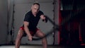 Assertive man doing exercises with battle rope, ruthlessly effective workout.