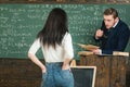 Assessing student learning outcomes. Teacher listen to girl student in classroom. Rear view woman in jeans answer to man