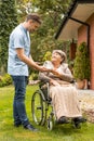 Assistant giving cup of tea to happy senior woman in the wheelchair in the garden Royalty Free Stock Photo