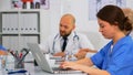 Assistant typing on laptop meeting informations while doctors discussing Royalty Free Stock Photo