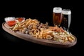 Assorted beer snacks. crackers, fried pieces of meat, french fries, chicken wings, sauces with two glasses of beer.