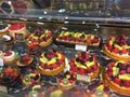 Assorted cakes topped with fruit displayed behind glass supermarket bakery section to entice customers to buy