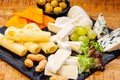 Assorted cheese on a black ceramic kitchen board with grapes, olives and nuts.Different types of cheeses on black board. Royalty Free Stock Photo