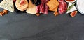 Assorted cheeses and meat appetizers, above view top border banner on a dark stone background with copy space