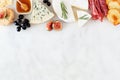 Assorted cheeses and meat appetizers, overhead view top border on a white marble background with copy space