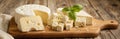 Assorted cheeses on a wooden board featuring a large round cheese, sliced cubes with herbs, and triangular wedges. Fresh basil Royalty Free Stock Photo