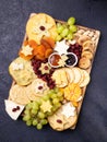Assorted cheeses on wooden board plate hard cheese slices, walnuts, grapes, crackers, chutney mango, jam, dark background, top