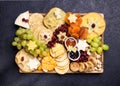 Assorted cheeses on wooden board plate hard cheese slices, walnuts, grapes, crackers, chutney mango, jam, dark background, top