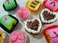 Assorted colorful cakes, including mini roll cakes and heart-shaped cakes with cream and sprinkles on a white table Royalty Free Stock Photo