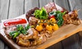 Assorted delicious grilled meat and vegetables with fresh salad and bbq sauce on cutting board on wooden background close up