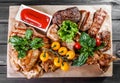 Assorted delicious grilled meat and vegetables with fresh salad and bbq sauce on cutting board on wooden background close up Royalty Free Stock Photo